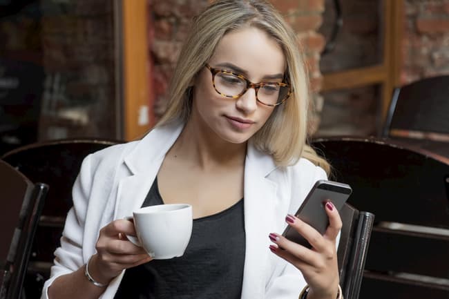 Junge Frau mit Handy und einer Tasse Kaffee.